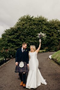 Bride holds bouquet in the air while walking though the grounds of Sherbrooke Castle Glasgow