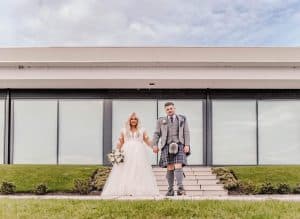 The bride and groom hold hands outside the lochside wedding venue